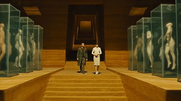 Blade Runner 2049 picks up these hints from the original and runs with them. It’s a visually gorgeous film, panning, as it opens, a vast cityscape in ambient sfumato, architecture somewhere between Albert Speer, Bauhaus, and I. M. Pei. Sans-serif text reveals that replicants have seen improvements: there’s now a model with an extended life span, another capable of complete obedience. The opening scene ends with an obedient one, a Blade Runner called K (Ryan Gosling), carrying a bloody eyeball in a plastic bag toward his police-issue hover car parked in the sand.